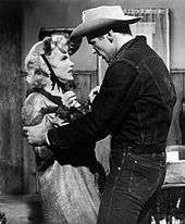Monroe and Don Murray in Bus Stop. She is wearing a ragged coat and a small hat tied with ribbons and is having an argument with Murray, who is wearing jeans, a denim jacket and a cowboy hat.