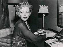 Monroe, wearing a transparent lace robe and diamond earrings, sitting at a dressing table and looking off-camera with a shocked expression