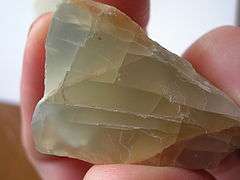 A chunk of grayish yellow moonstone which shows fracture lines and a blue glow in some portions.