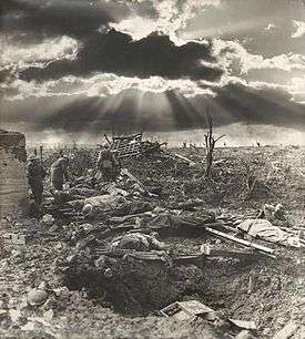 a sunburst through the clouds is shown against a landscape of destroyed land with a shellholes.
