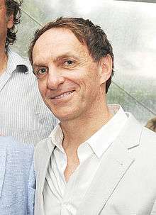 A man with light brown hair wearing a white coat and a white collared shirt.
