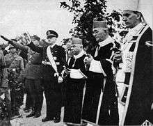 three priests and several saluting males in military uniform