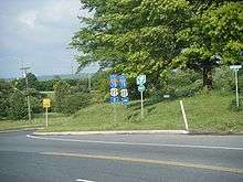 A three lane surface road at an interchange with an Interstate highway. A set of signs on the right side of the road reads west Interstate 78 U.S. Route 22 straight ahead, east Interstate 78 U.S. Route 22 right, and New Jersey Turnpike right