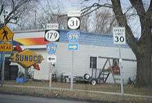 Two adjacent road signs at a T-intersection with the left sign reading north Route 179 Hunterdon County Route 579 with a left arrow and the left sign reading south Route 31 Hunterdon County Route 579 with a right arrow. A Sunoco gas station lies in the background