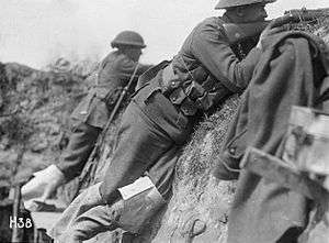 A black and white photograph of two men in military uniform pointing rifles over the lip of the trench in which they are standing