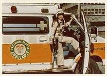 Nancy Caroline in jumpsuit in front of the orange ambulances used in Pittsburgh in the 1970s for Freedom House.