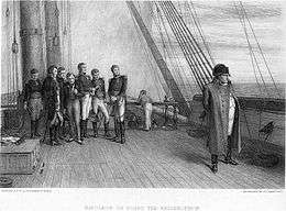 Napoleon standing alone on a sailing vessel with a group of his officers watching him intently
