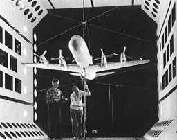 Two men testing a scale model airplane in a wind tunnel.
