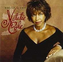 A woman is shown in a black dress in front of a brown background. On the left-hand side of the picture, the words Natalie Cole are written in a large, red, cursive font over the images of holly and ivy. The words Holly & Ivy are written in a smaller, green font above this.