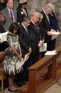 From left to right: the Obamas, and two other couples stand with their heads bowed in a pew
