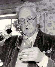 monochrome photograph of a man, wearing glasses and holding a brandy glass