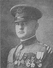 Head and shoulders of a white man in a military uniform with a long row of medals across his left breast, a strap lying diagonally across his chest, a high, stiff, collar, and a peaked cap.