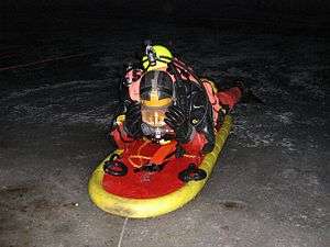 A diver wearing a dry suit skidding on the ice surface, on a special platform, at night.