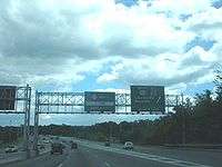 A freeway at an exit with two green signs over the road. The one on the left reads Route 23 north U-turn next right while the one on the right reads south U.S. Route 202 Alt County Route 511 Lincoln Park Boonton Service Road with an arrow pointing to the upper right.