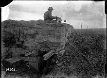 a man sitting a top a partially destroyed concrete bunker with a box in his hand.