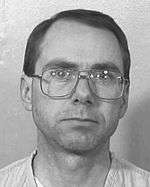 black and white photograph of a white male in his mid 30s, with thinning black hair, thick eyebrows, wearing very large, thick glasses with square frames