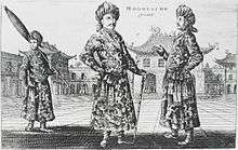 A black-and-white print depicting three standing men wearing turbans, a long robe with a sash, and shoes with rising pointed tips, against an architectural background of buildings with roofs that point upwards. The man on the left, slightly in the background, is carrying a long folded umbrella on his left shoulder. The one in the center, who faces the viewer, is resting on a cane. The man on the right, seen in profile view, faces the center man.