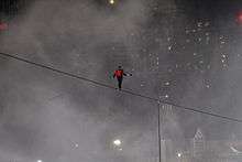 A man on a tightrope with mist and lights in the background