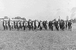 Rows of men in light-coloured military uniforms and pith helmets in a field