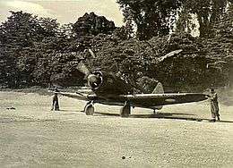 Single-engined military monoplane with propeller spinning, on jungle airfield