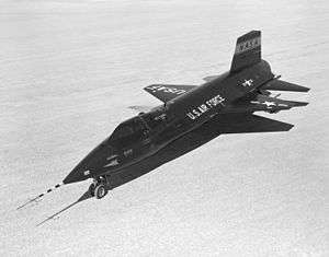 Black rocket aircraft with stubby wings and short vertical stabilizers above and below tail unit