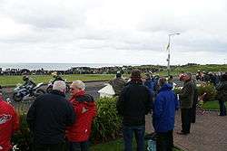 Spectators standing in the front garden of a house watching the motorcycle racing.