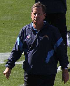 Candid waist-up photograph of Turner walking on a football field wearing a dark blue San Diego Chargers jacket