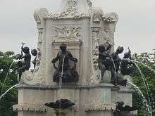 six black statues on an ornate white stone structure. Waterjets are emerging from their nipples and various other places