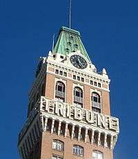 A clock tower on top of a brown building with the word "TRIBUNE" written across it.