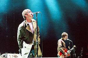 A color photograph of Noel and Liam Gallagher of the band Oasis on stage
