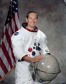 man in space suit, hands on globe, American flag in background