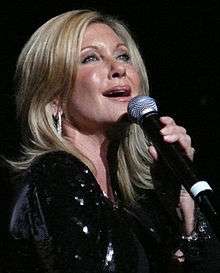 A woman with blond hair in black clothing, holding a microphone