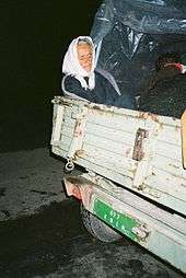 An elderly woman sitting in the back of a utility trailer