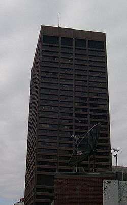 Ground-level view of a rectangular skyscraper with a dark brown facade and prominent black windows