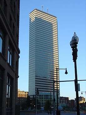 Ground-level view of a 45-story building with a trapezoidal footprint, a white facade and black windows