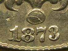 A closeup of part of an 1873 Shield nickel; the arms of the "3" curve only slightly towards each other