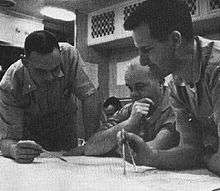 Three naval officer plotting the submerged course of the nuclear submarine Triton, with Captain Beach seated before chart in the center, with Lt. Commander Will M. Adams standing at right holding a pair of dividers and Lt. Commander Robert W. Bulmer standign at the left holding a pencil, and an unidentified individual seated in the background.