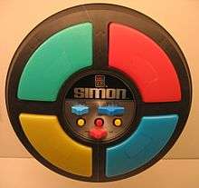 The game is a circular disc divided into four quarter circle buttons each with a different color. In the center are the game mode controls