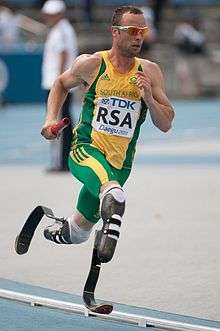 A disabled Caucasian sprinter running on running blades, he wears the green and yellow of South Africa.