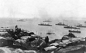 A group of large warships steaming slowly off a city.