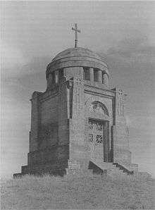 The Ostrach battle monument is a small, square building, raised from the ground about .5 meter, 8 meters high. A 3 meter dome, topped with a simple cross, caps the monument. It is of marble, with a simple double door.