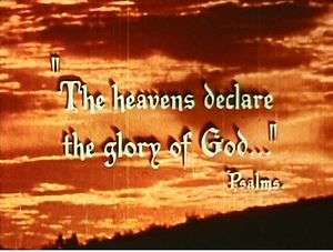 The quotation "The Heavens Declare the Glory of God" and credit "Psalms" are overlaid against a photograph of an orange sky and clouds; there is a dark hillside sloping across the bottom right of the photograph. The impression is of a photograph taken at sunrise. The typeface used for the quotation has a Gothic style.