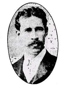 Man with short dark hair parted in middle with long moustache wearing a suit in an oval frame