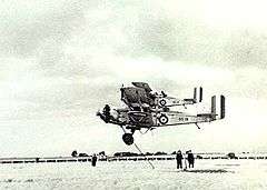 Military biplanes flying low over a field