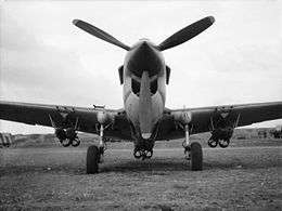 Low-angle front view of single-engined military aircraft with three-bladed propeller and six bombs beneath the wings and fuselage