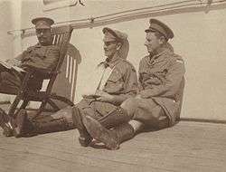 An informal group portrait of three military officers sitting on the deck of a ship.