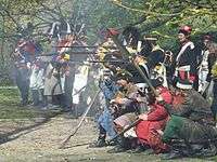 A group of reenactors dressed in Polish 18th century uniforms and szlachta civilian attire firing a musket volley.