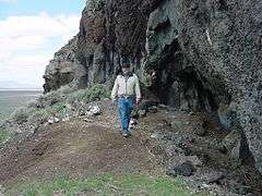 Photograph of a man walking at the base of a cliff