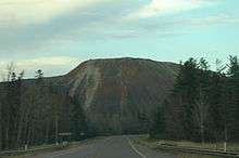 A roadway leading away into the distance before curving in front of a large pile of waste rock