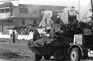 photograph of a Marine LAV-25 and utility truck in the foreground with a partially destroyed building in the background